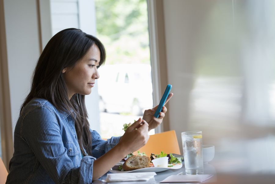 Frau checkt ihr Smartphone, während sie einen Salat isst